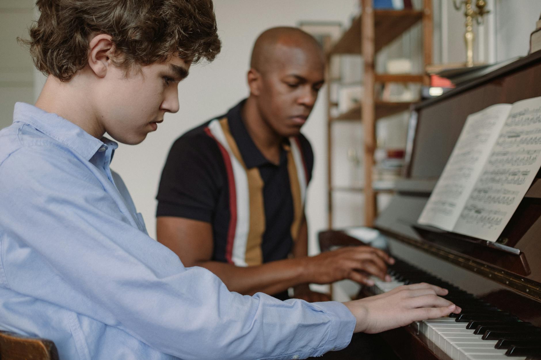 teacher and teenage boy sitting by piano